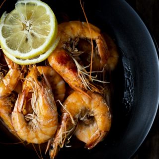 head on shrimp in a bowl with lemon slices.