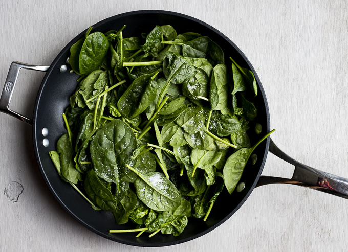 raw spinach in a skillet with salt