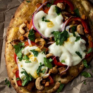 naan pizza with melted cheese, red pepper, cilantro, cashews and yellow sauce