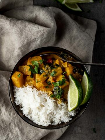 a bowl of orange butternut squash curry with rice and sliced limes