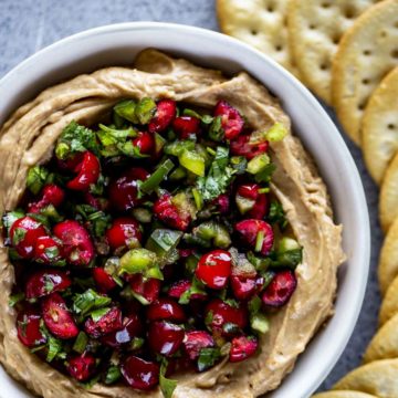 diced jalapenos and cranberries with cilantro over a cream colored dip with crackers on the side