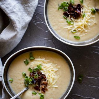 pureed cauliflower soup in bowls with spoons, bacon, green onions and shredded cheese