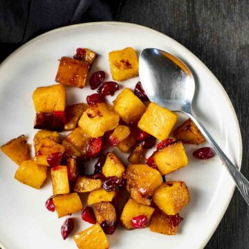 a plate of roasted butternut squash and cranberries with a spoon