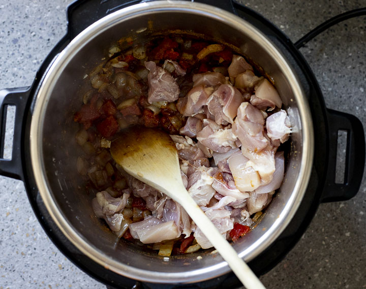 diced raw chicken cooking in a pot with vegetables.