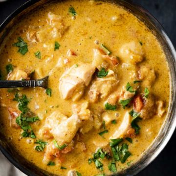 a bowl of orange chicken curry with a spoon