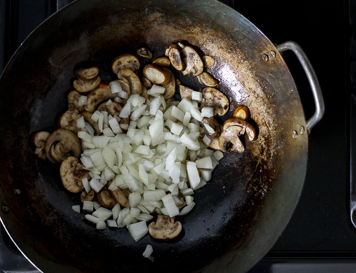 sliced mushrooms and diced onions in a wok.