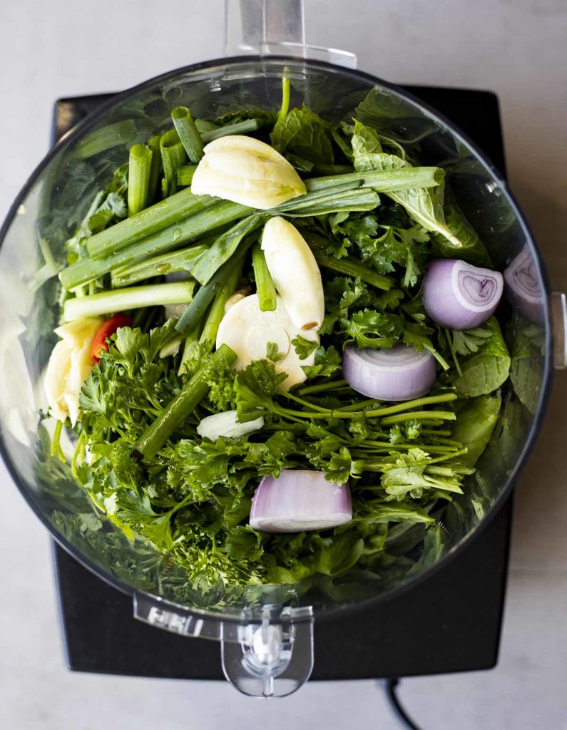 fresh green herbs, garlic and shallots in a food processor bowl