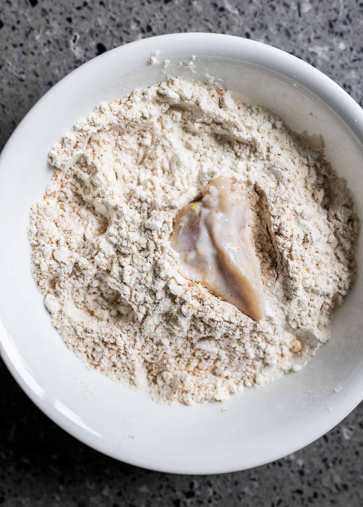 a piece of alligator being dipped in a flour mixture