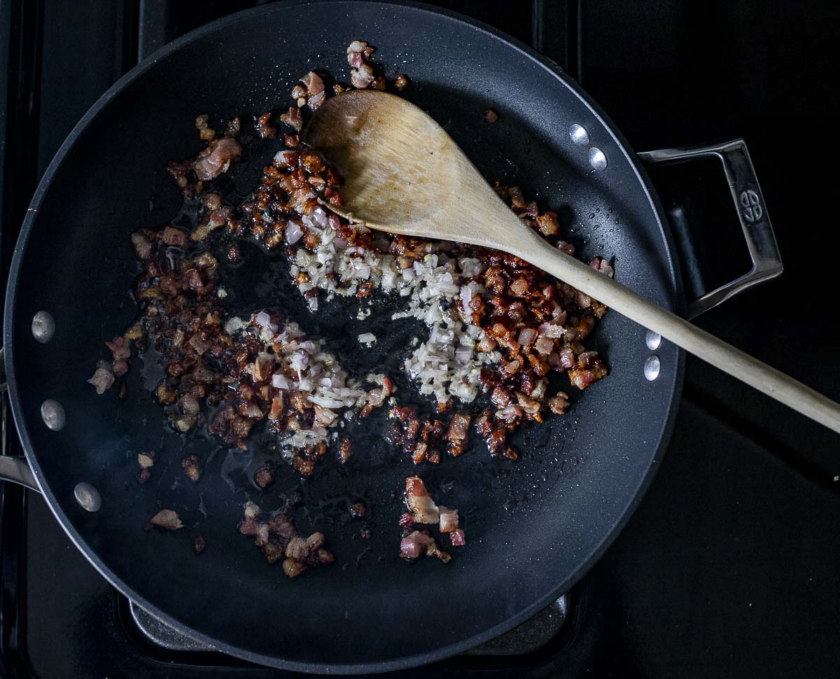 pancetta and diced shallots frying in a skillet.