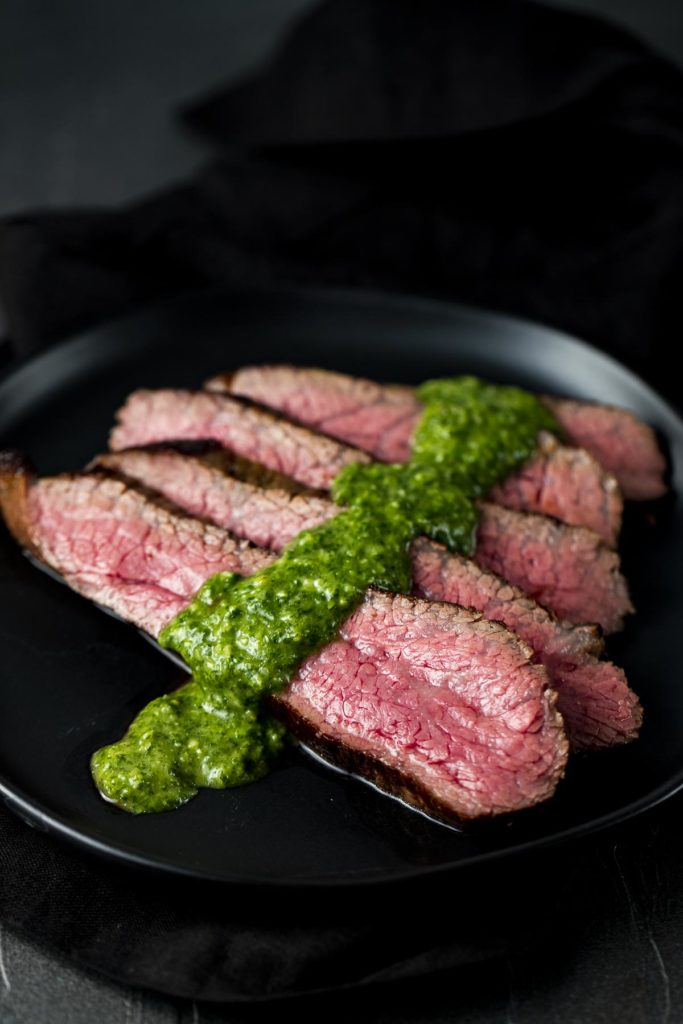 sliced beef on a plate with green sauce