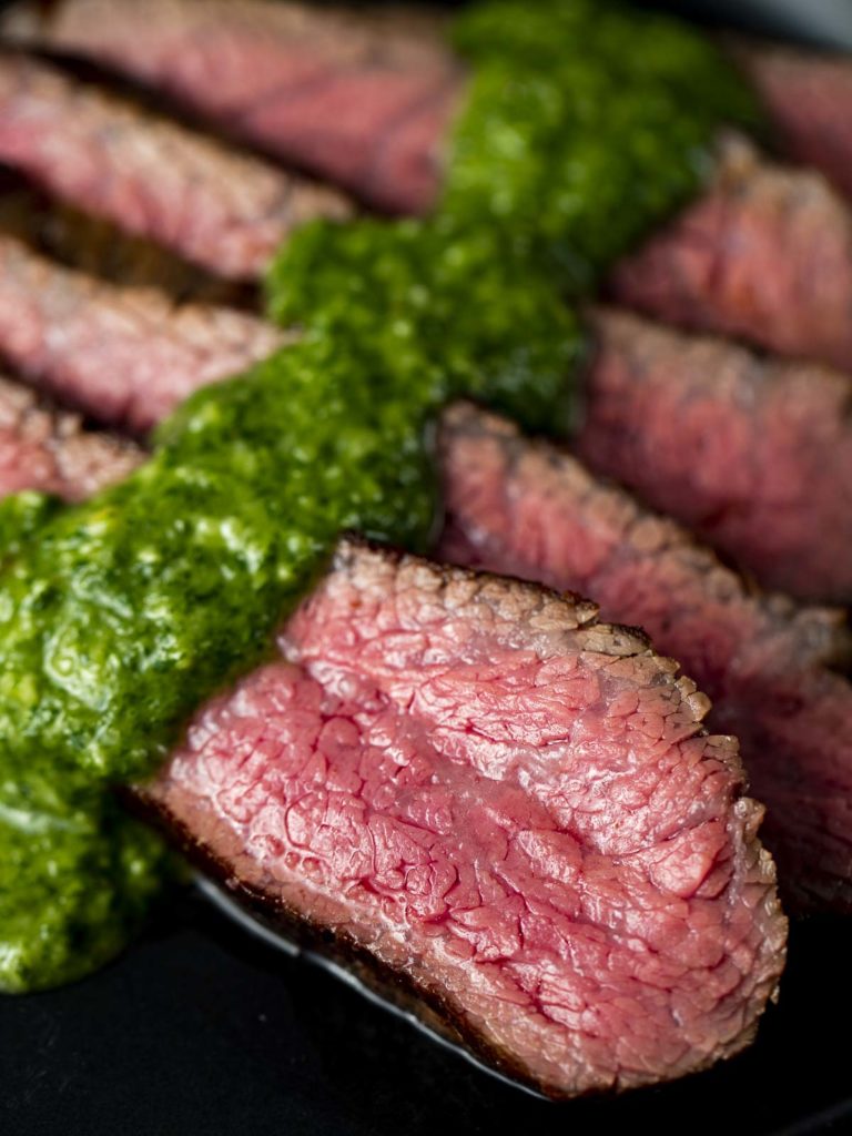 sliced beef with green chimichurri sauce on a plate