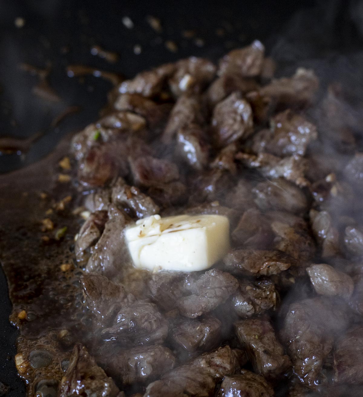 a pad of butter cooking with cubes of beef on a skillet.