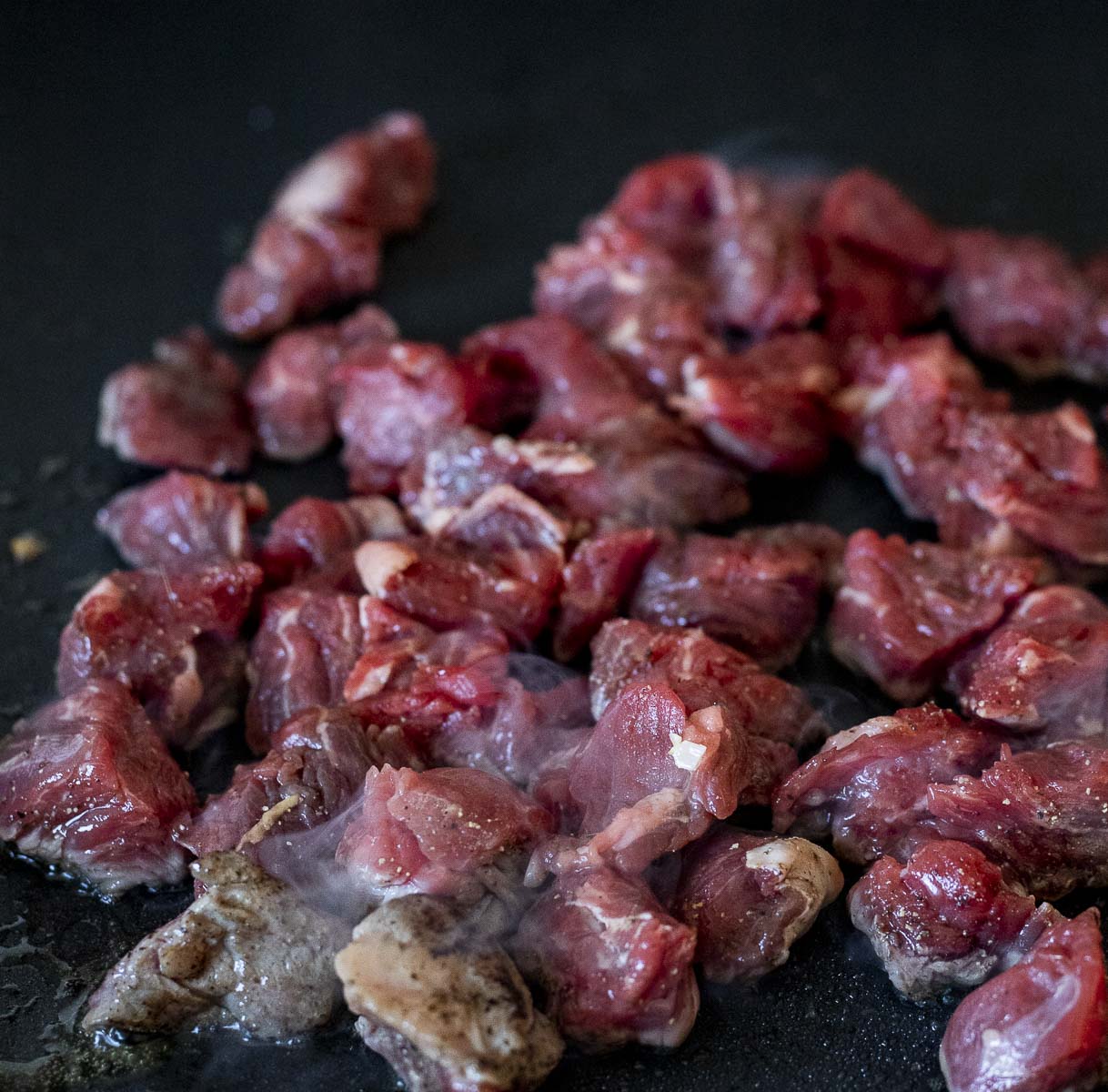 raw beef cubes cooking on a skillet.