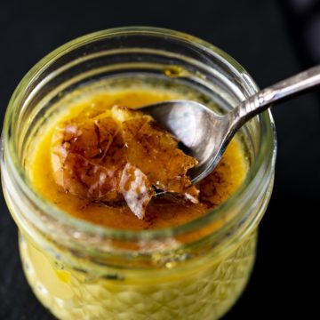 a spoon cracking the top of a glass jar of creme brulee