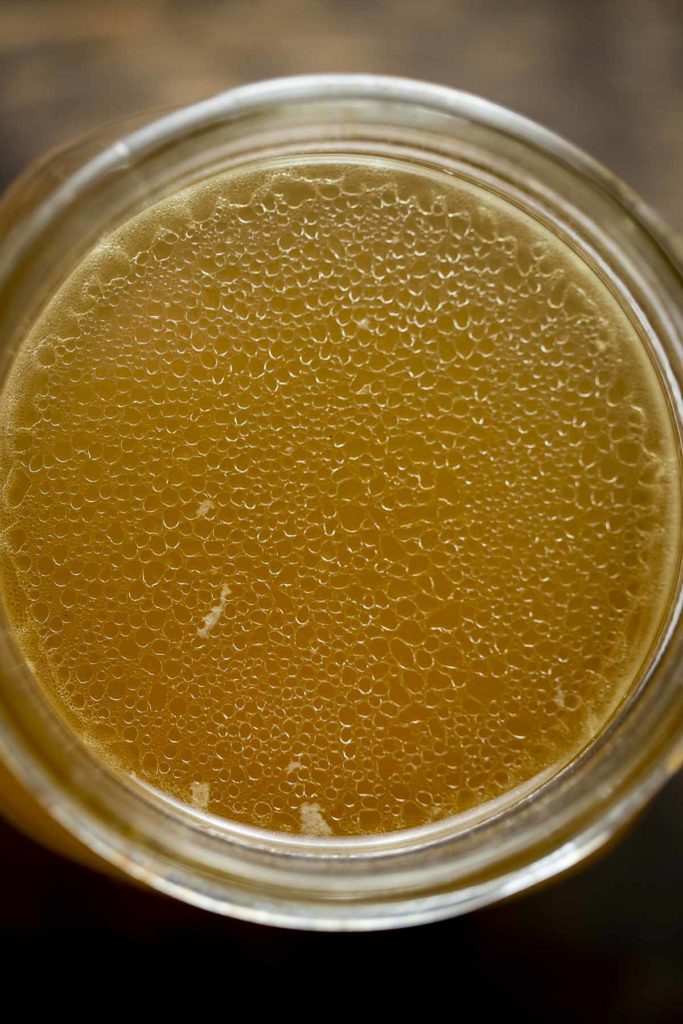 golden colored broth in a jar top down view