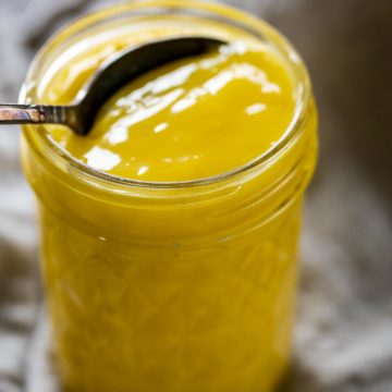 A mason jar of lemon curd with a spoon inserted.