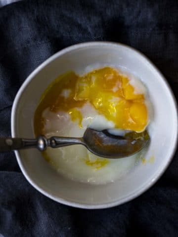 Overhead view of a poached egg in a bowl being eaten.