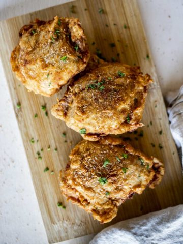 Overhead view of crispy chicken thighs on a wooden board.