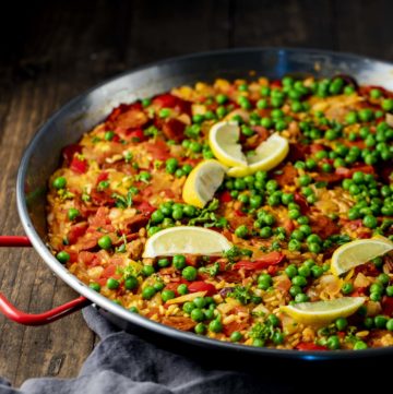 Side view of paella topped with green peas and lemon slices.