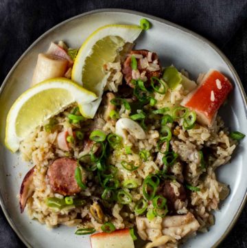 Overhead of seafood rice on a white plate with lemon wedges.