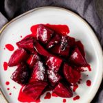 Overhead view of beet pieces with orange glaze on a white plate.