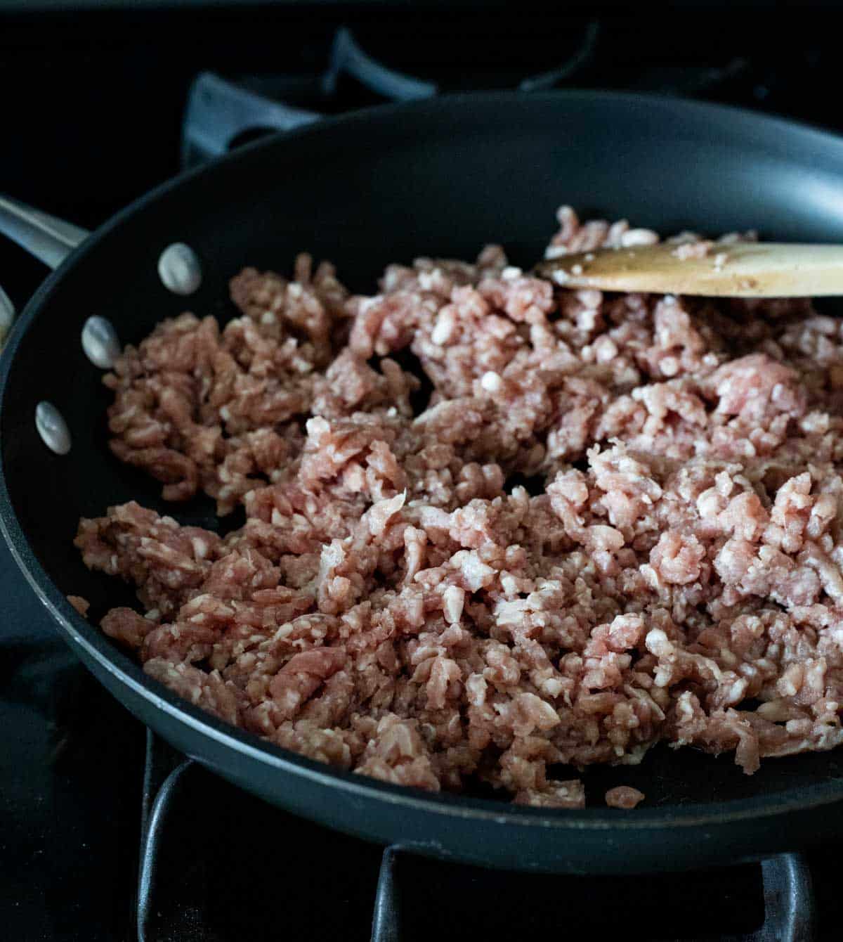 ground pork in a frying pan with a wooden spoon.