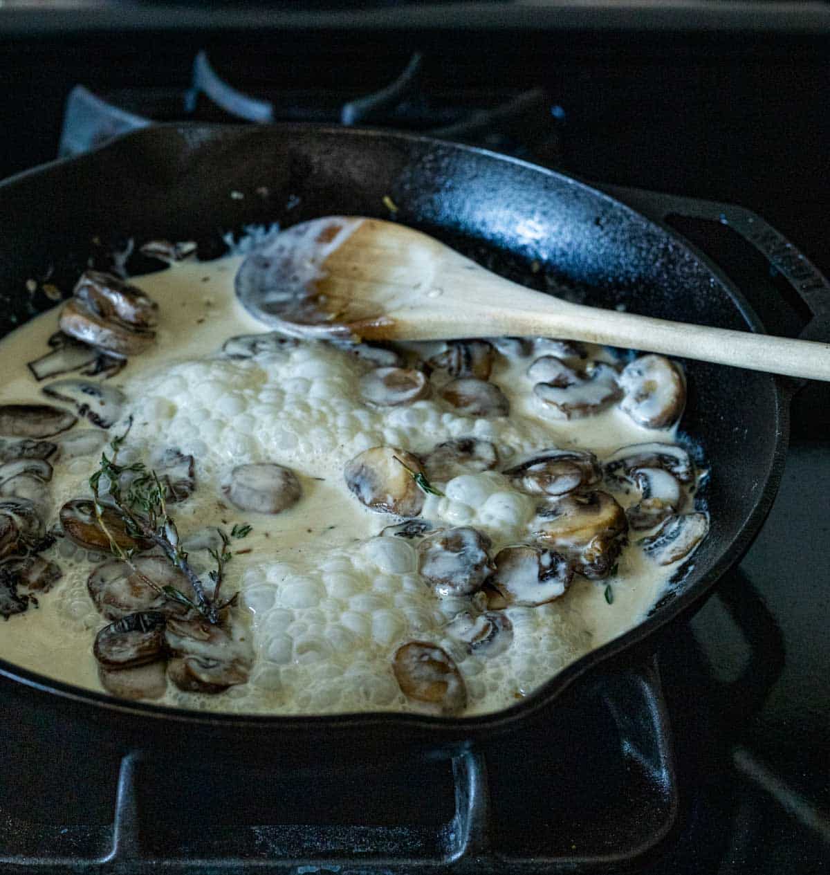 a creamy mushroom sauce simmering in a skillet with a wooden spoon