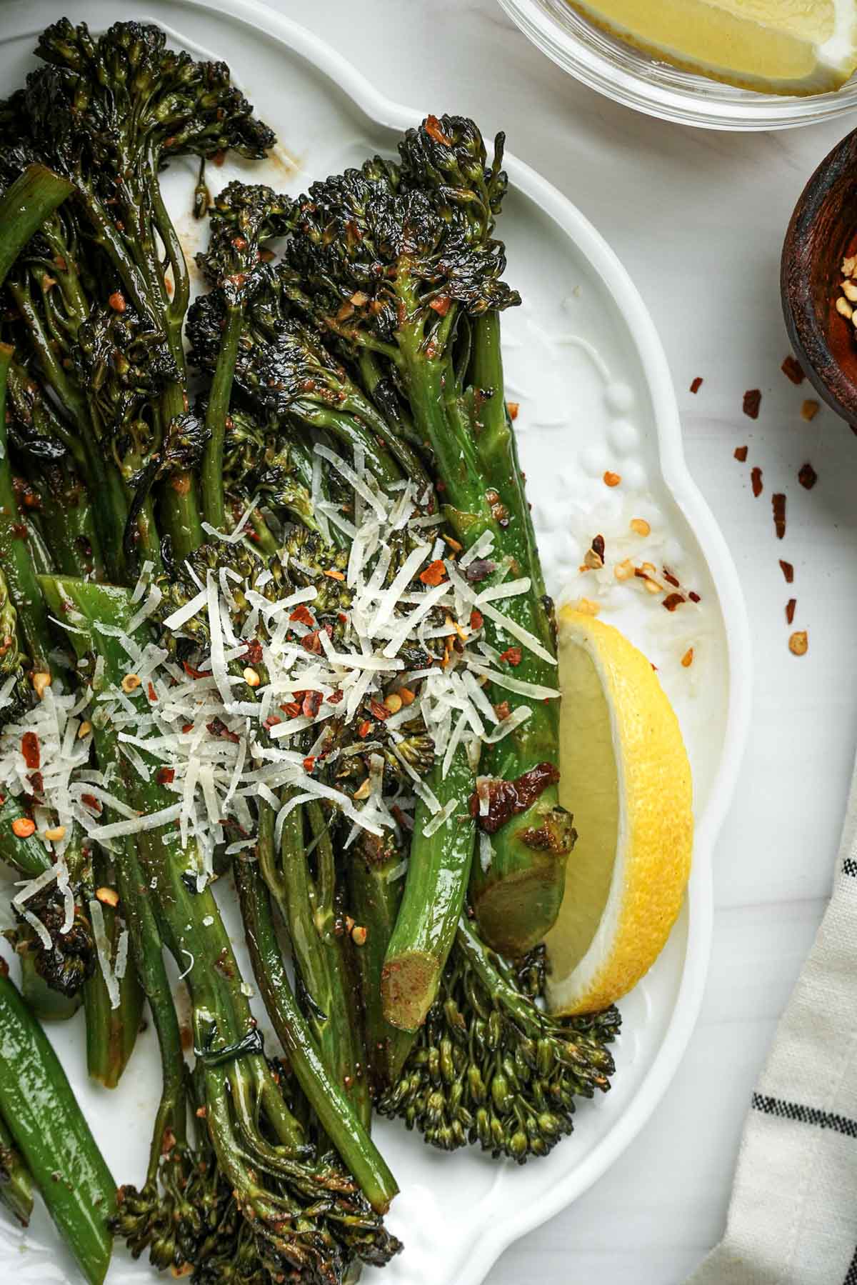 a plate of green vegetables with cheese and lemon wedges