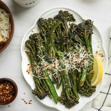 broccoletti on a plate with cheese, chilies and lemon wedge on the side