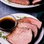 a plate of sliced roast beef with fresh thyme and a bowl of brown liquid