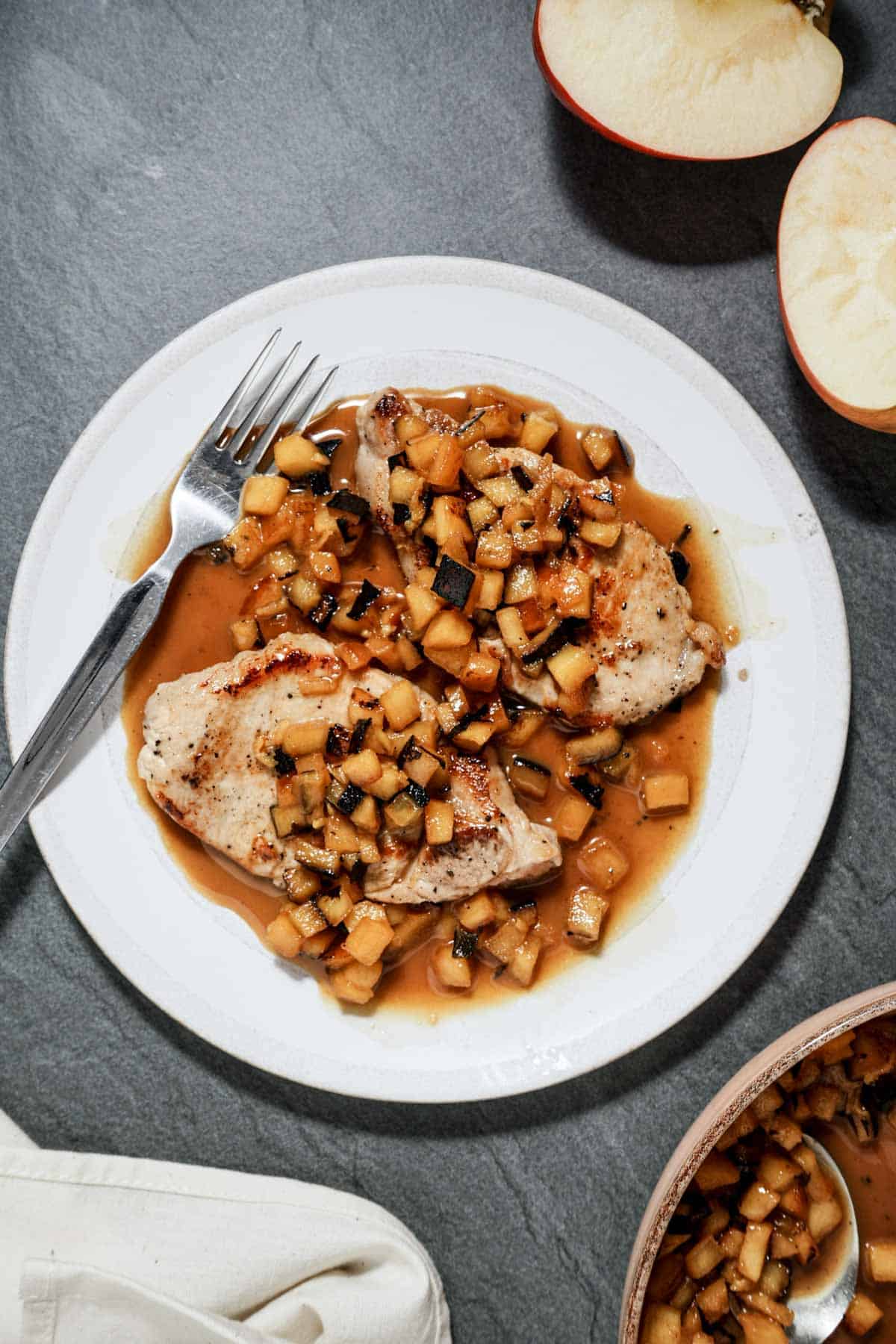 a plate of pork chops and sauteed apples with a fork