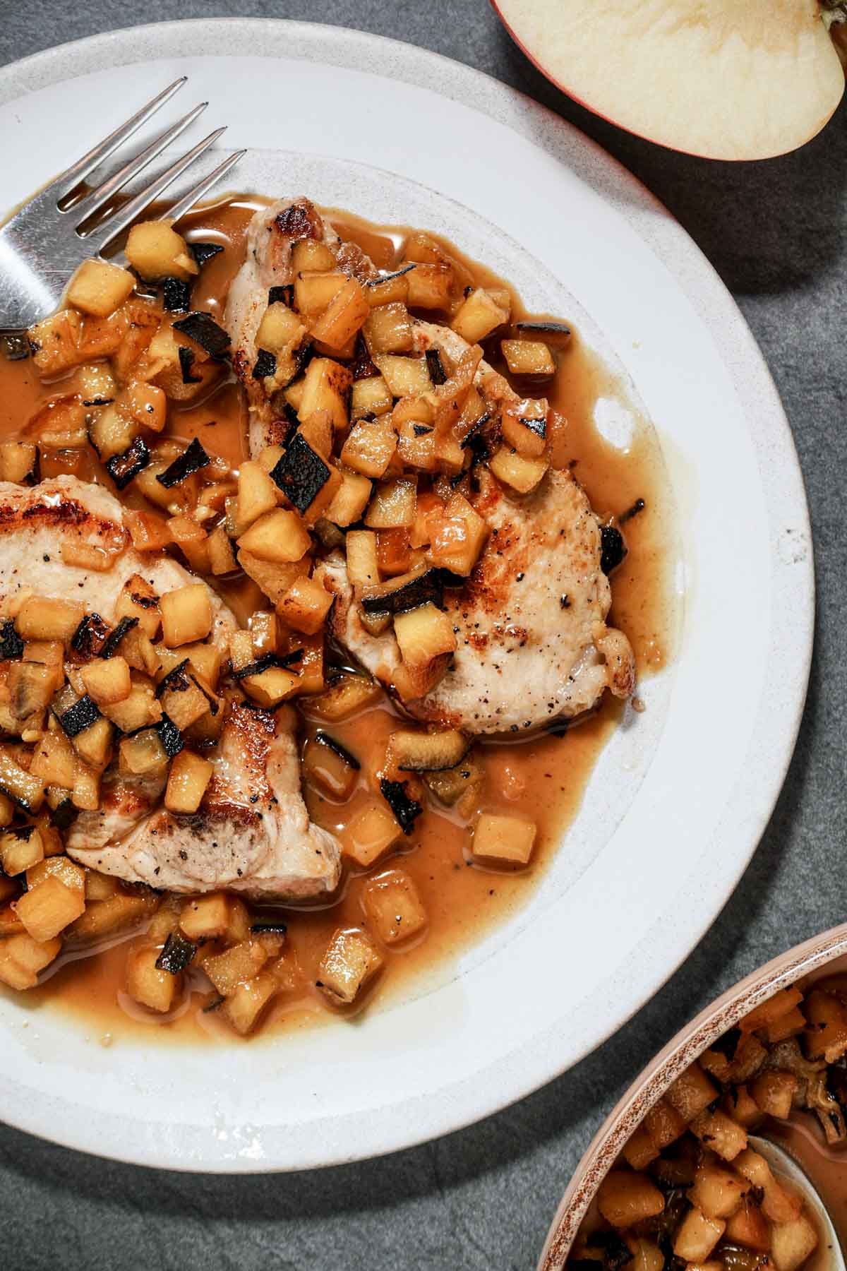 sauteed apple pieces in an orange colored sauce over top of 2 pork chops