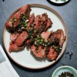 sliced beef and green onions on a white plate