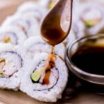 dark brown eel sauce being poured on a sushi roll