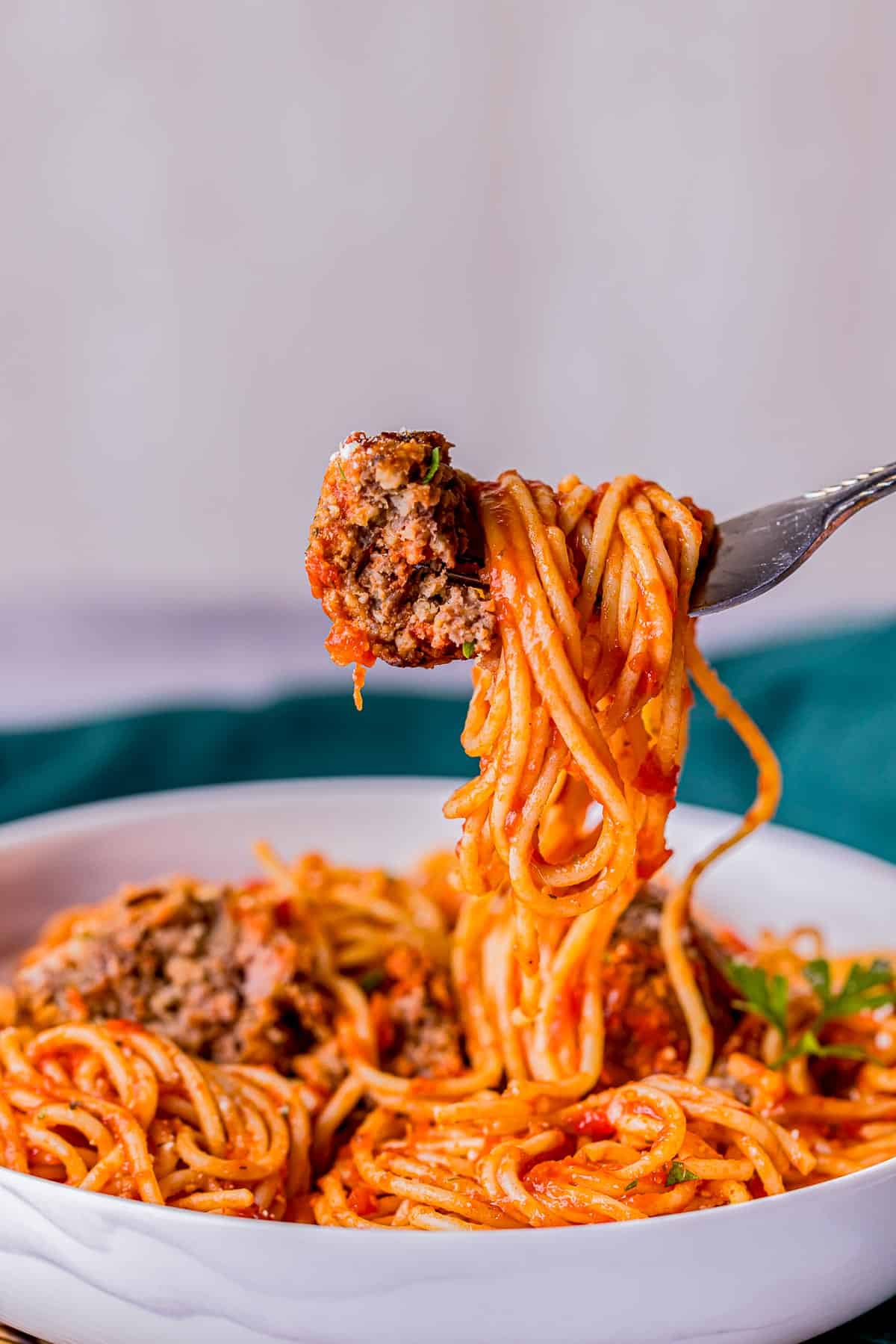 a fork of spaghetti with meatballs held up above a bowl