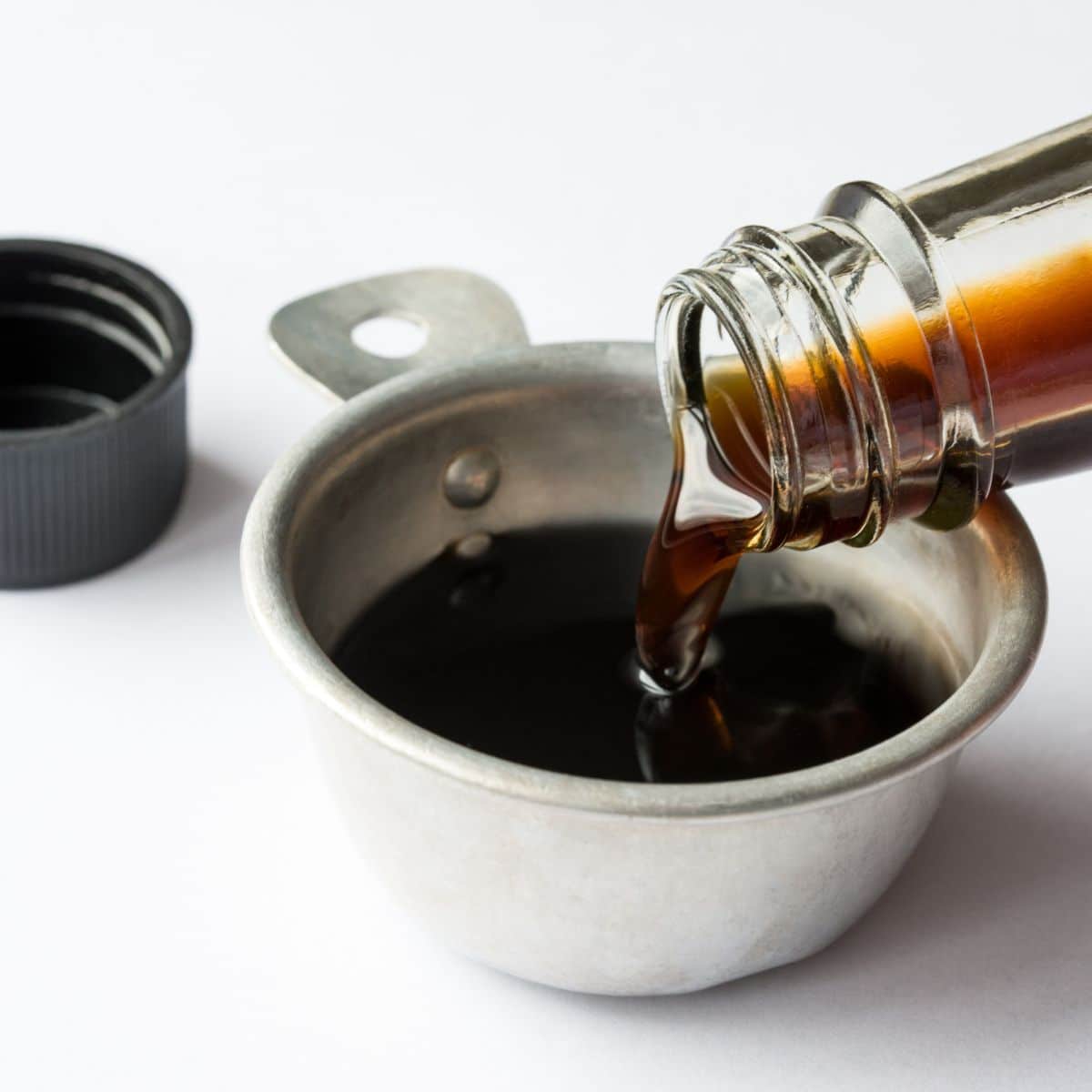 a glass bottle pouring soy sauce into a white bowl