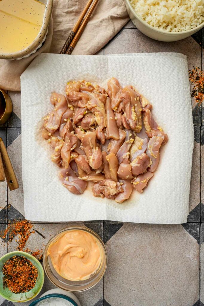 Raw chicken patted dry on a paper towel before frying