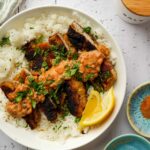 paprika schnitzen in a bowl with orange sauce, herbs, and lemon wedges