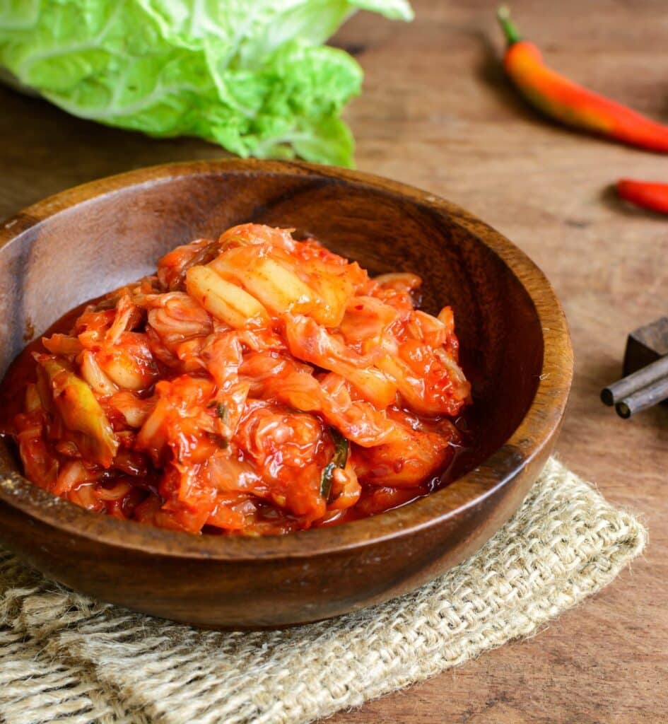 a bowl of red kimchi with chilies and lettuce in the back