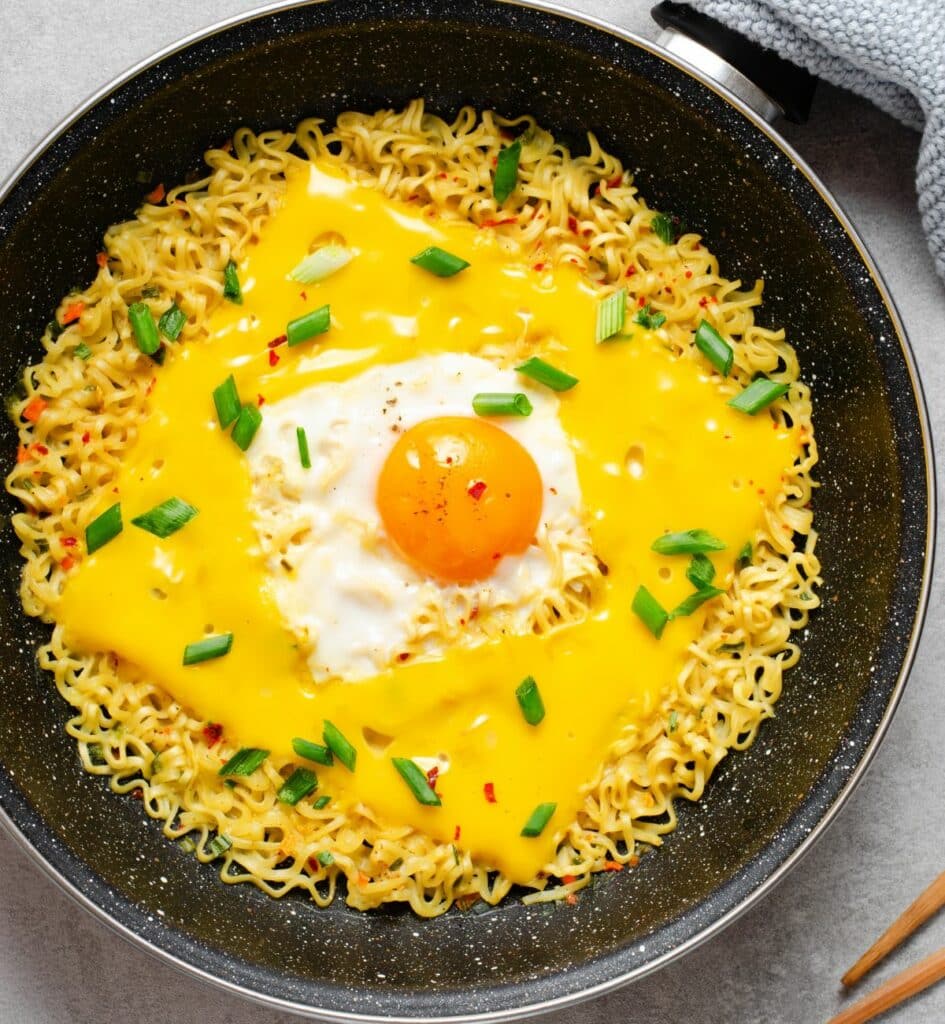 a bowl of cooked ramen noodles with melted american cheese and an egg on top