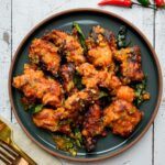 a plate of fried chicken and curry leaves in a sauce