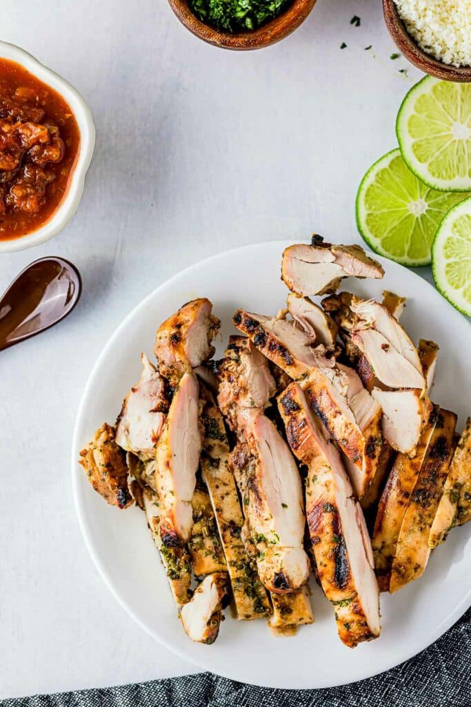 sliced chicken on a plate with salsa and limes on the side