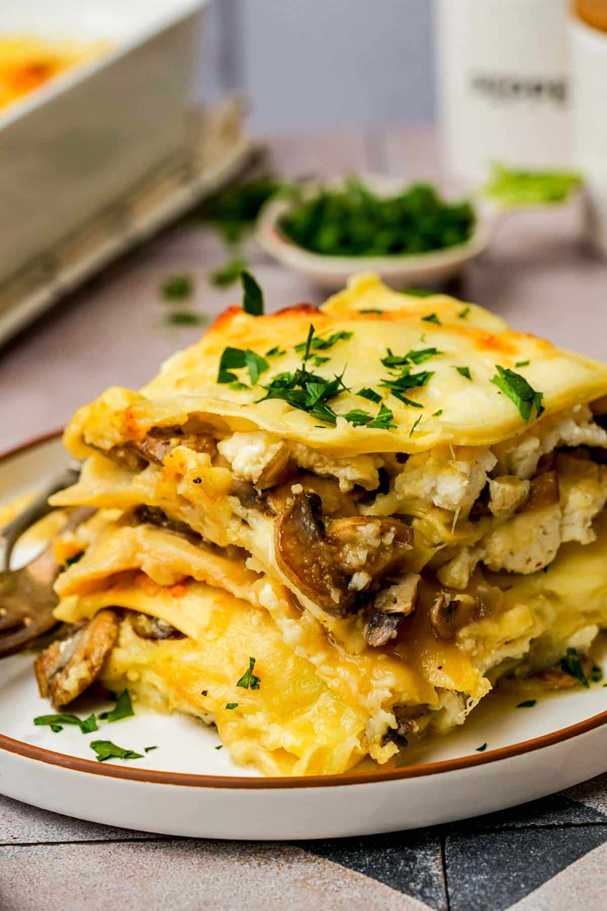 sliced mushroom lasagna on a plate garnished with herbs.
