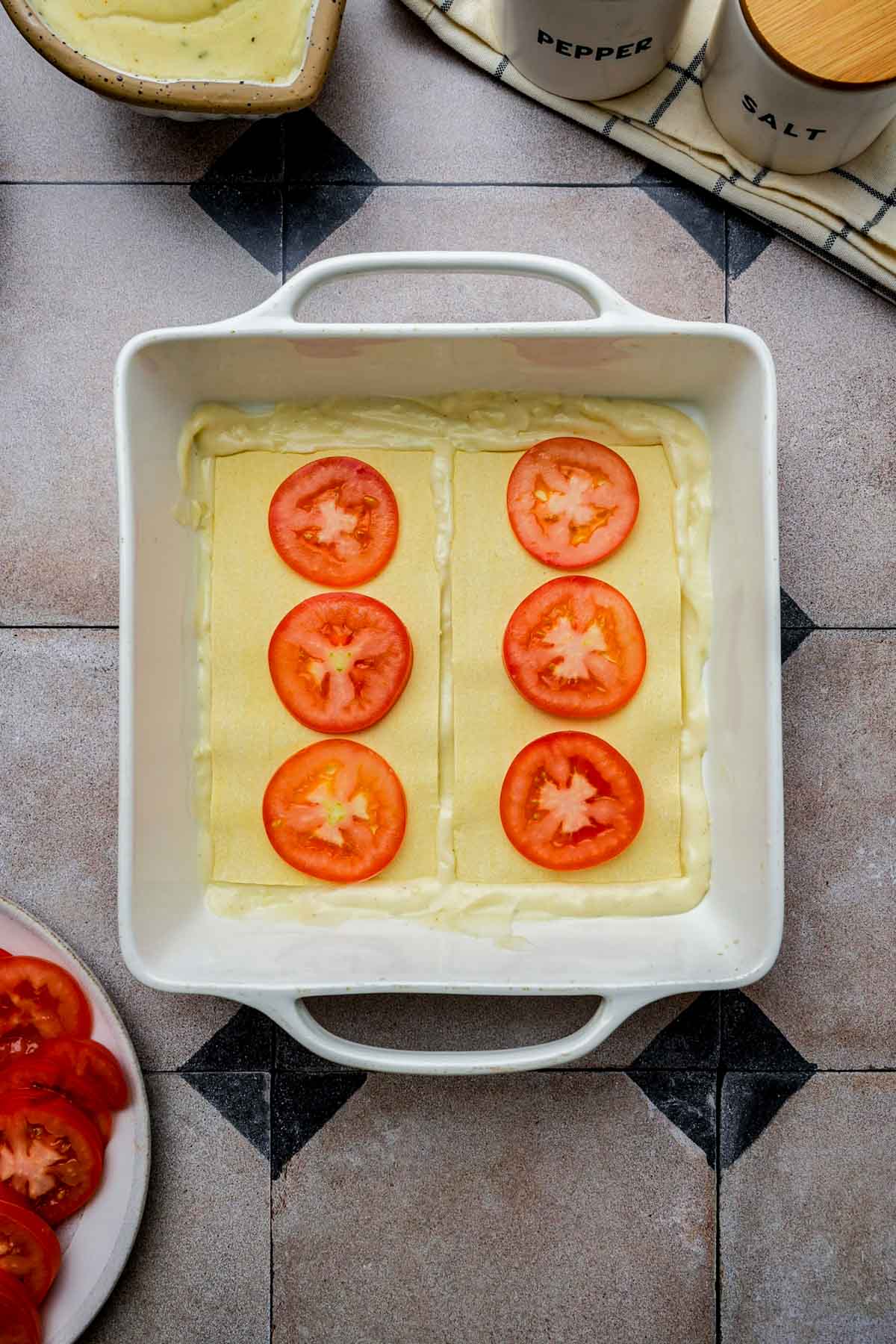 tomato slices on top of lasagna noodles in a pan.