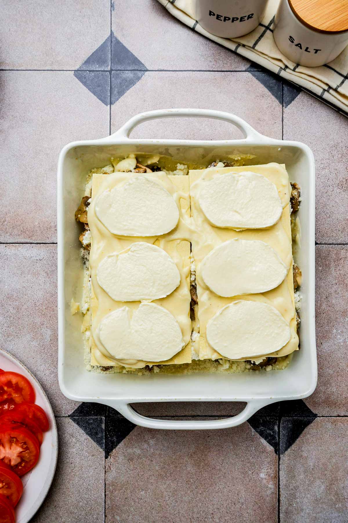 assembling mushroom lasagna with slices of mozzarella cheese in a pan.