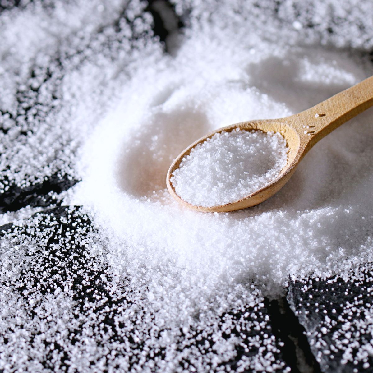 salt spread out on a dark surface with wooden spoon