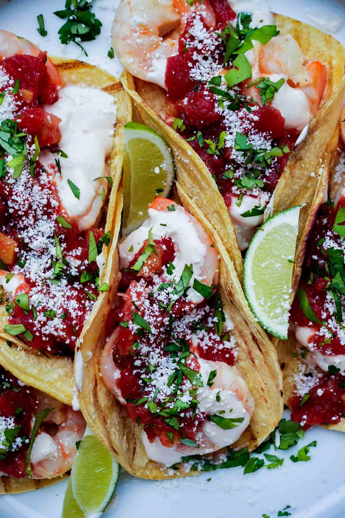 tacos de camaron on a plate with limes, cilantro and cheese.