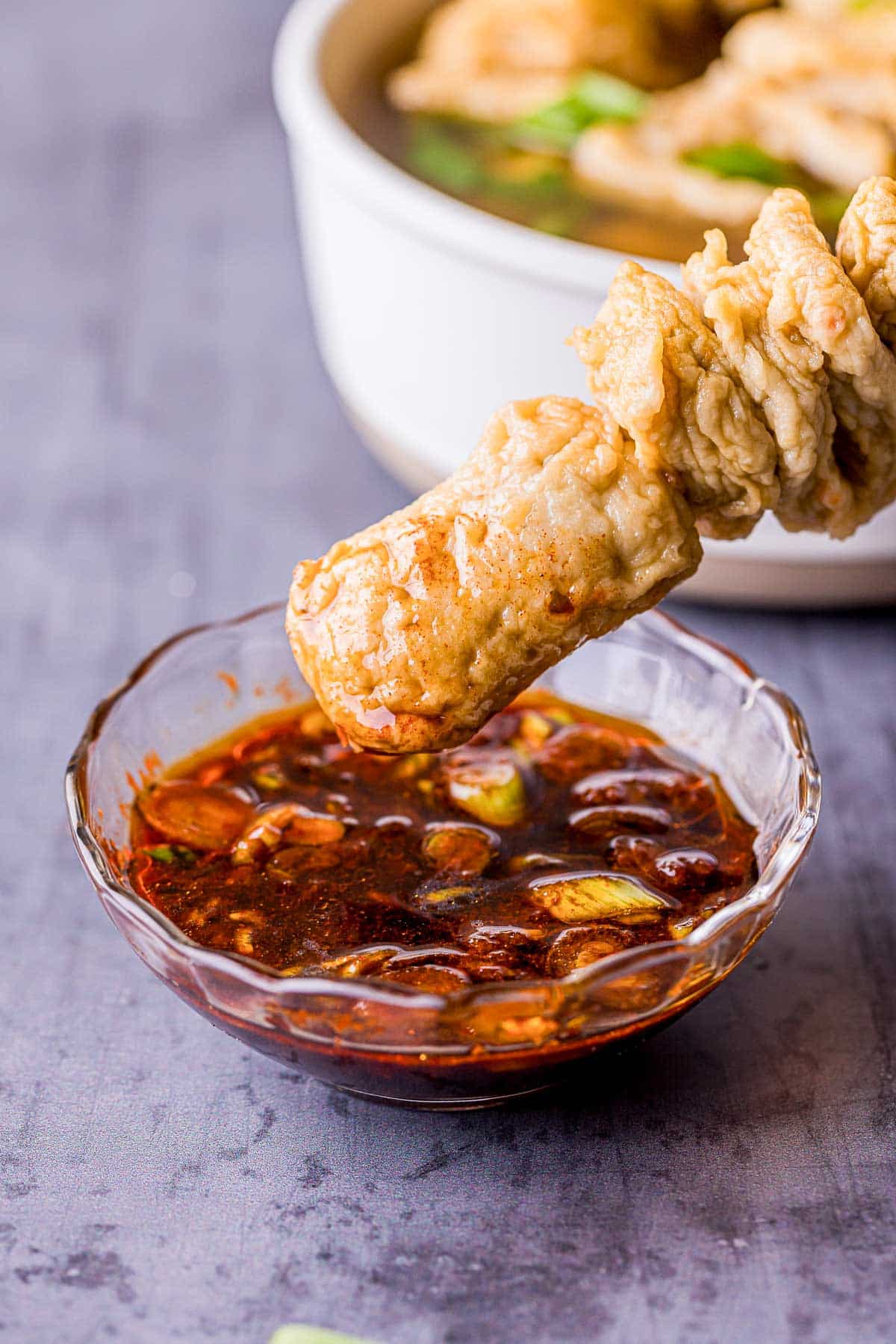 skewered fish cakes, or odeng, being dipped in a reddish sauce.