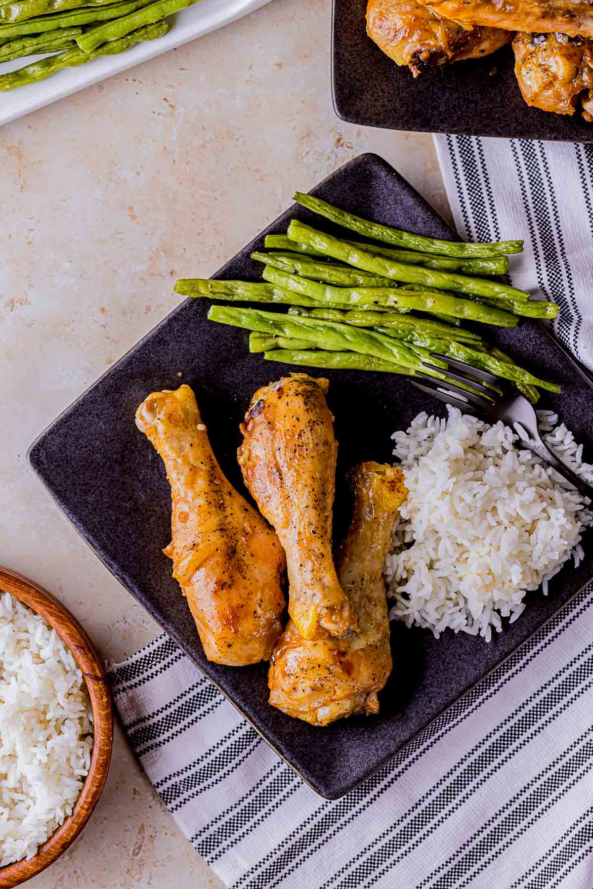 3 chicken drumsticks with white rice and green beans on the side.