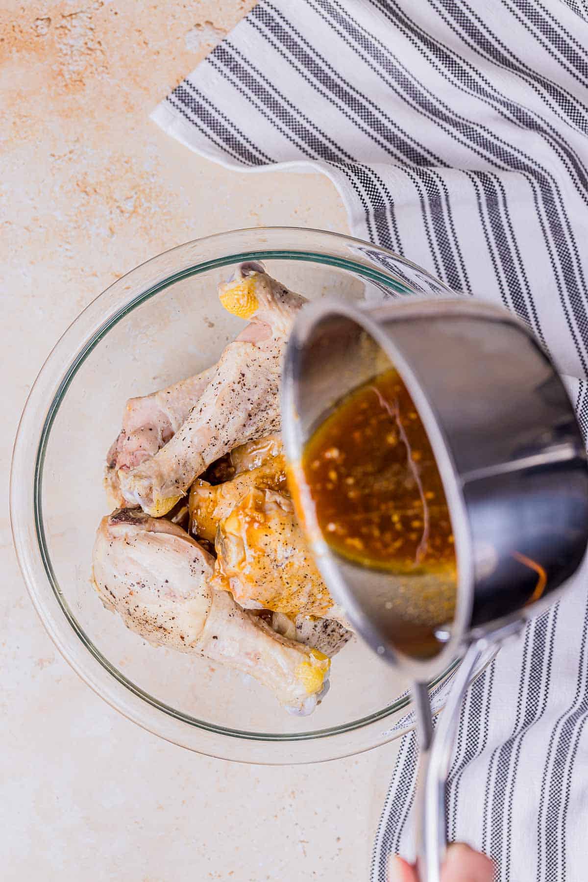 glaze being poured over chicken drumsticks in a bowl.